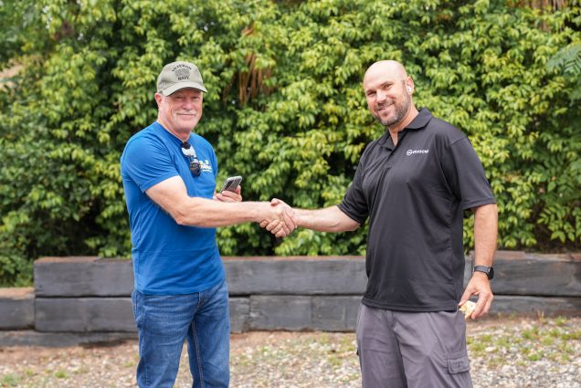 Grasons employee shakes hands with a new franchise owner in front of a leafy green bush